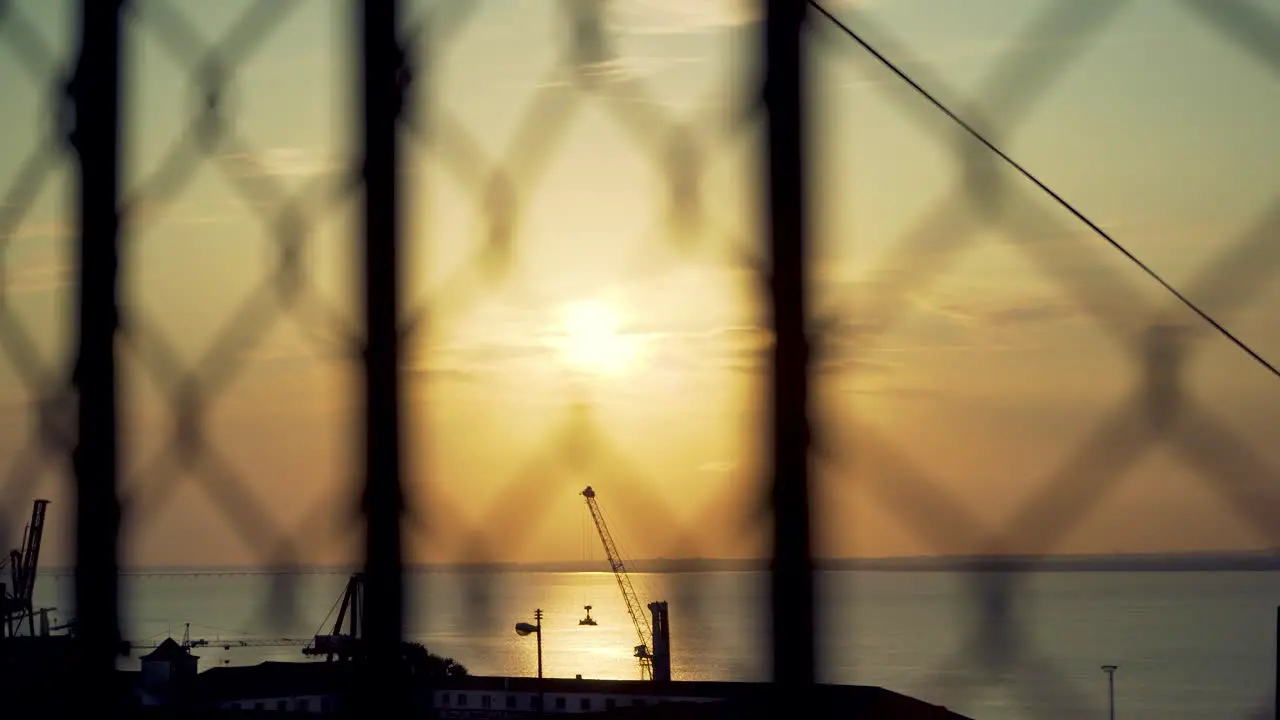 Lisbon harbor sunrise with cranes silhouette through out of focus wire fences