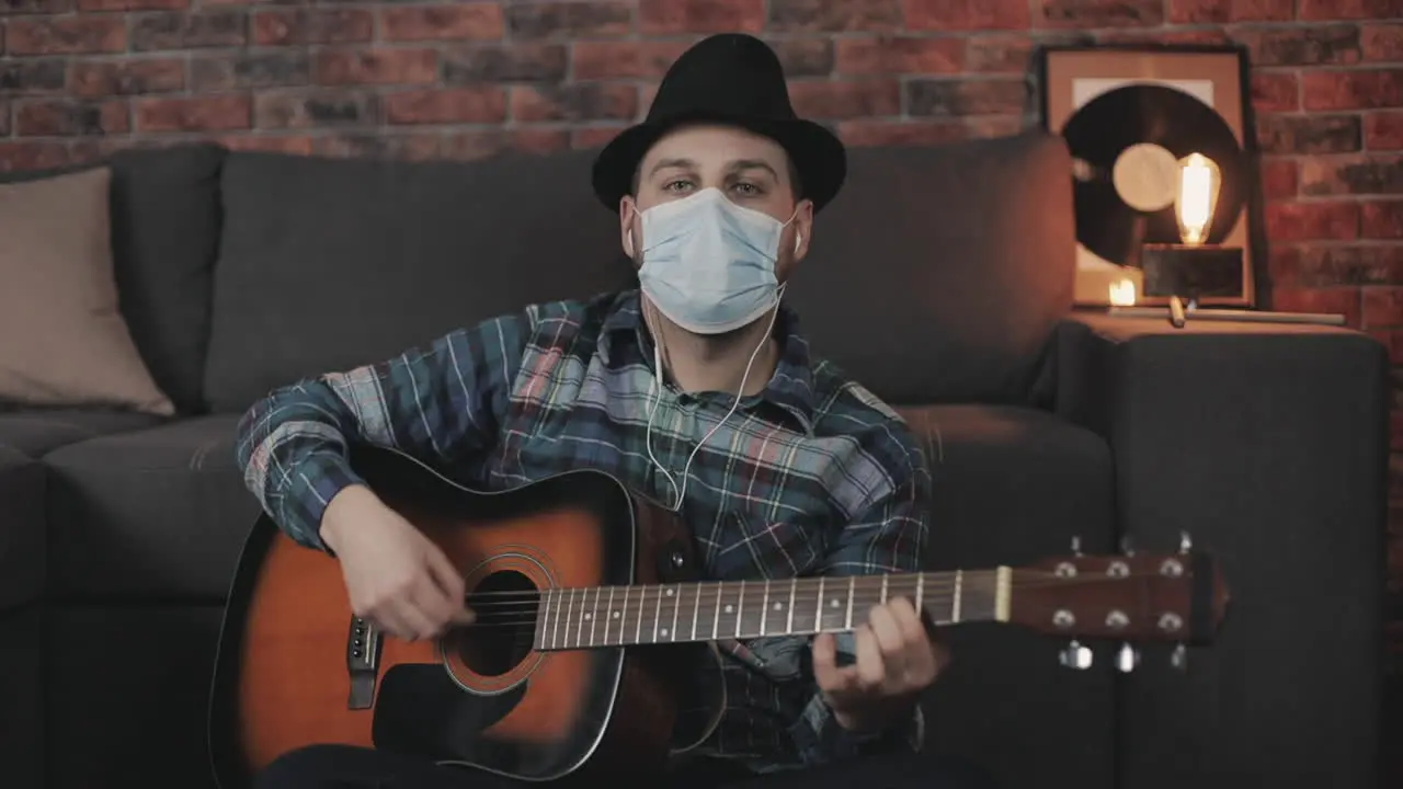 Portrait Of Young Male Musician With Medical Face Mask Playing Guitar Looking At Camera At Home During Lockdown Due To The Covid 19 Pandemic