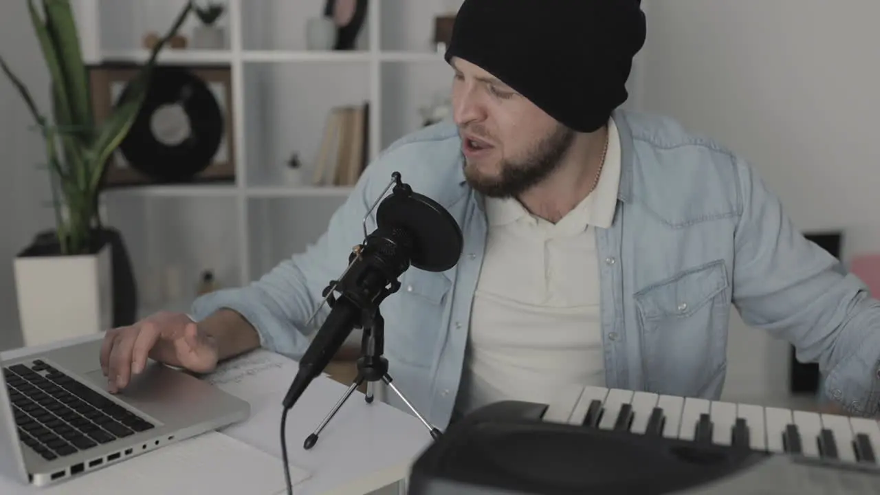 Male Musician Singing Playing Electric Keyboard And Using A Laptop At Home