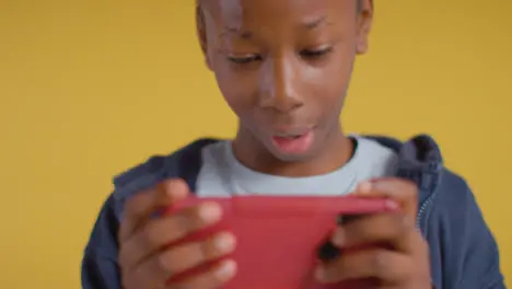 Close Up Of Excited Boy On ASD Spectrum Gaming On Mobile Phone On Yellow Background 