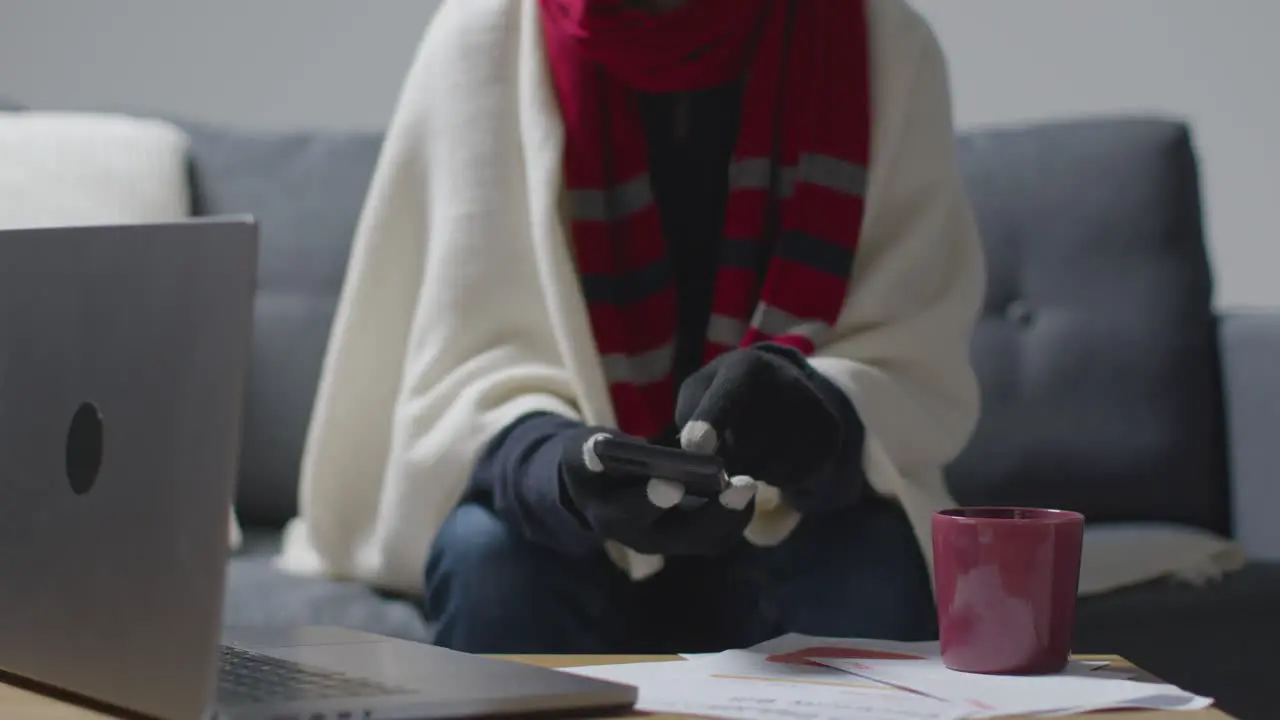 Person Wearing Blanket Using Phone Sitting On Sofa At Home Trying To Keep Warm In Energy Crisis