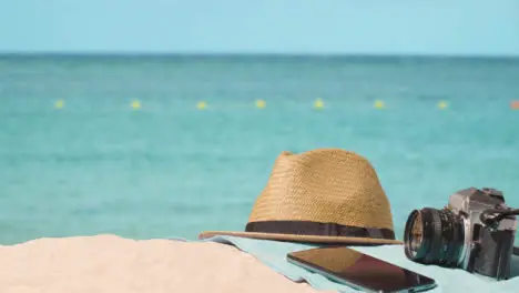 Summer Holiday Concept Of Camera Sun Hat Mobile Phone Beach Towel On Sand Against Sea