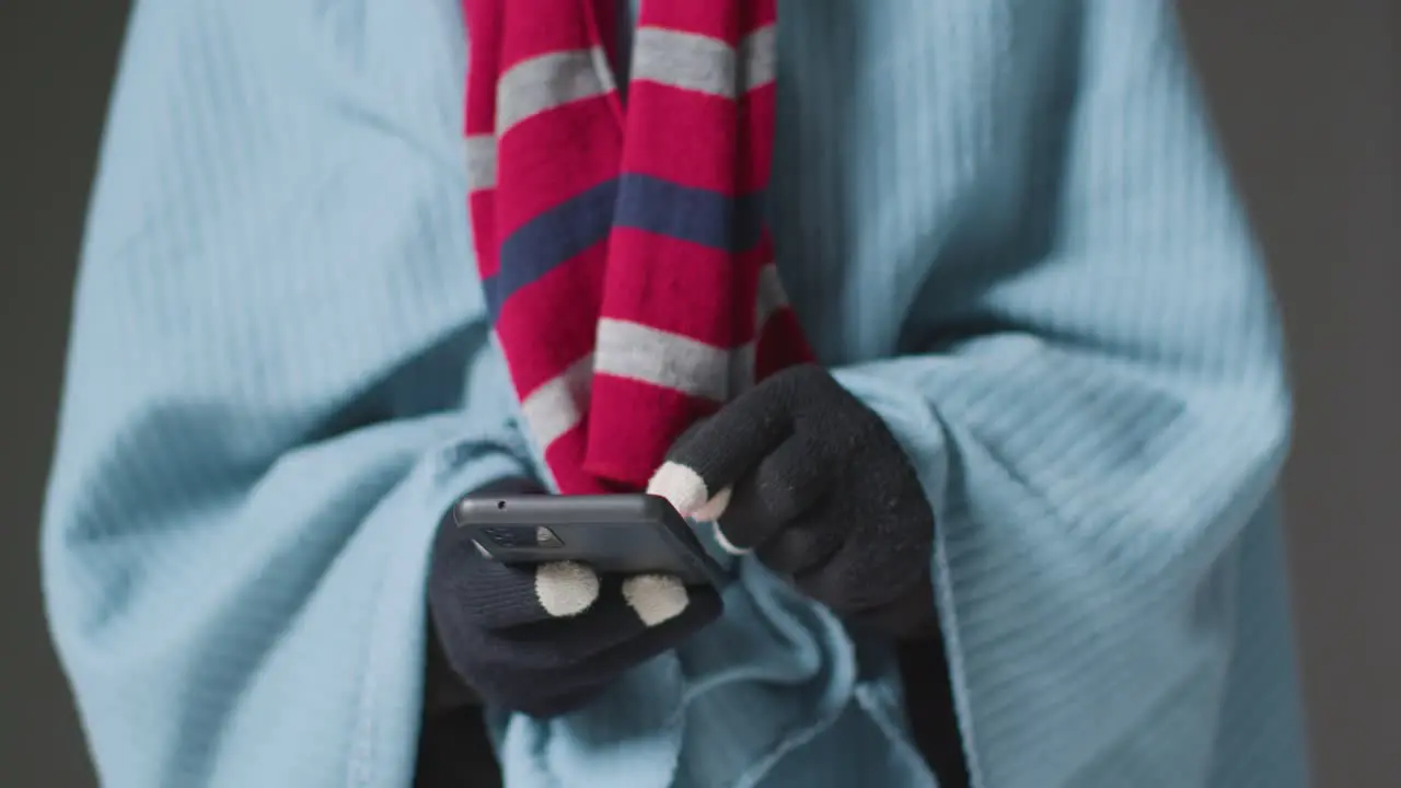 Close Up Of Person Wearing Blanket With Hot Drink Using Mobile Phone Trying To Keep Warm In Energy Crisis 4