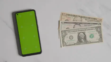 Overhead Currency Shot Of Hand Grabbing US Dollar Bills Next To Green Screen Mobile Phone