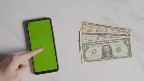 Overhead Currency Shot Of US Dollar Bills Next To Person Using Green Screen Mobile Phone