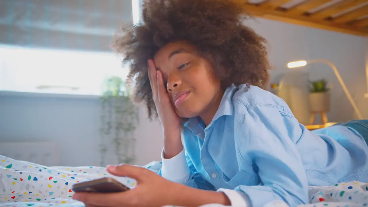 Tired Or Worried Boy In Bedroom Lying On Bed Holding Mobile Phone Being Bullied Online