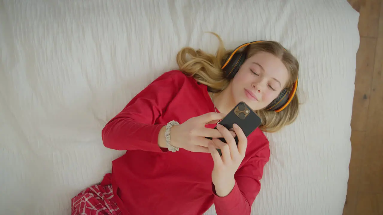 View from above of teenage girl wearing wireless headphones streaming music or film from mobile phone -s hot in slow motion