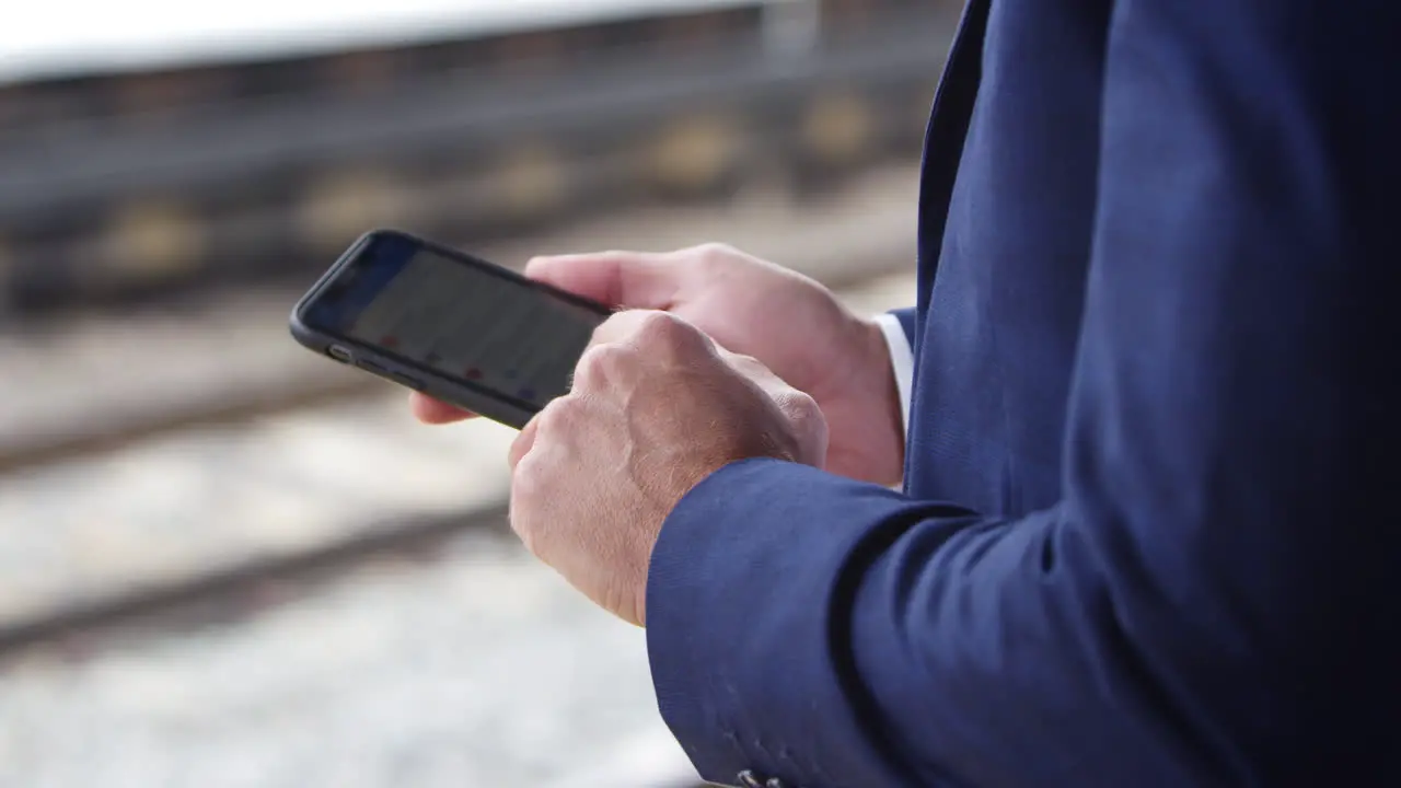 Close Up Of Businessman On Railway Platform Texting On Mobile Phone