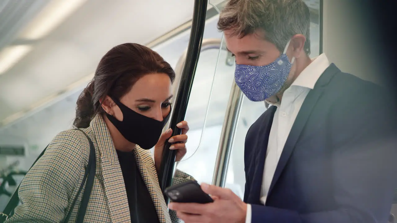 Business Commuters Stand In Train Carriage With Mobile Phones Wearing PPE Face Masks During Pandemic