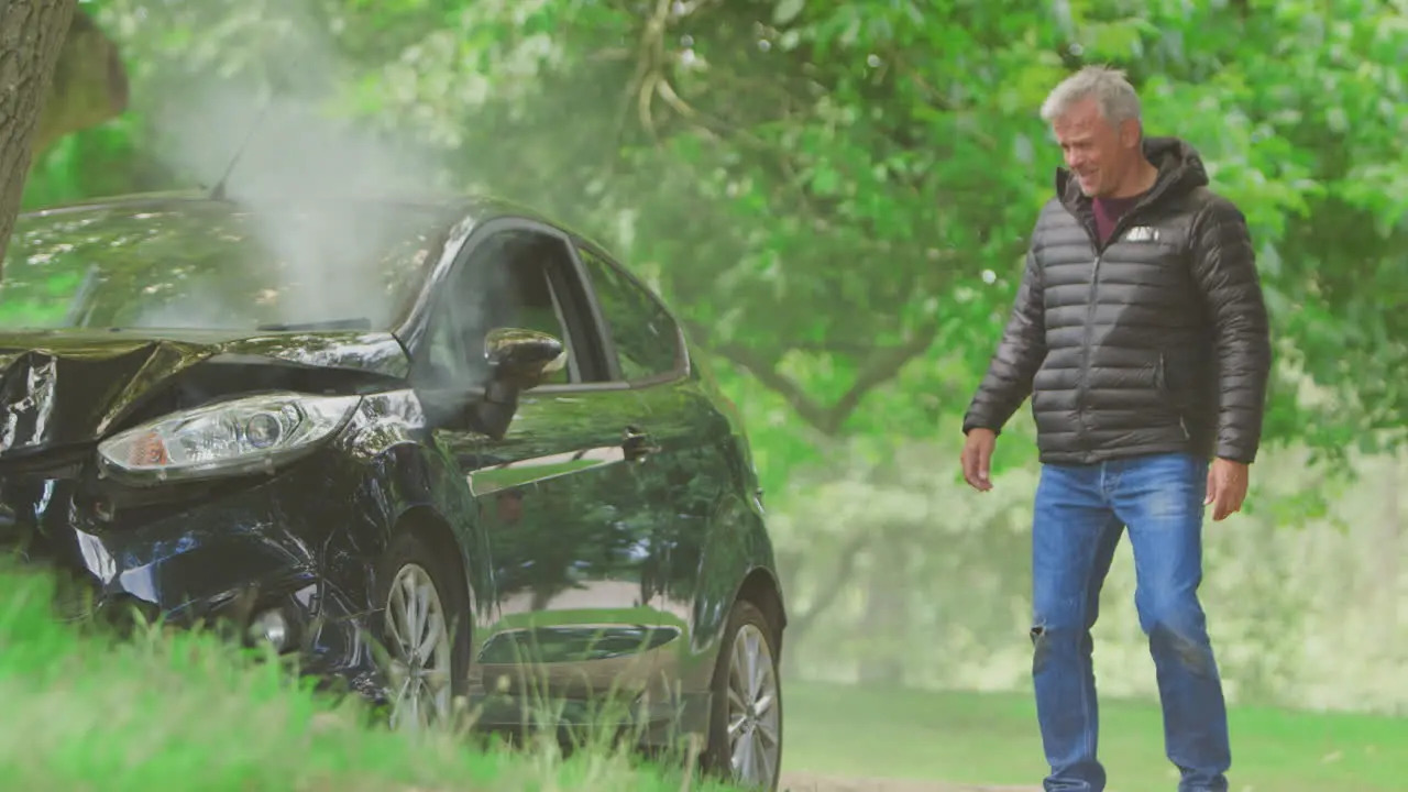 Mature Man Gets Out Of Smoking Car And Takes Photo Of Accident Damage On Mobile Phone