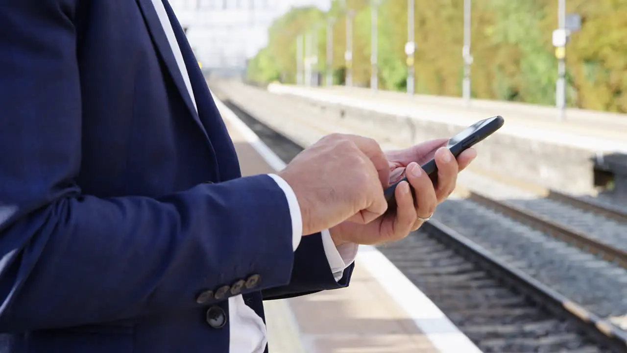 Close Up Of Businessman Standing On Railway Platform Using Mobile Phone