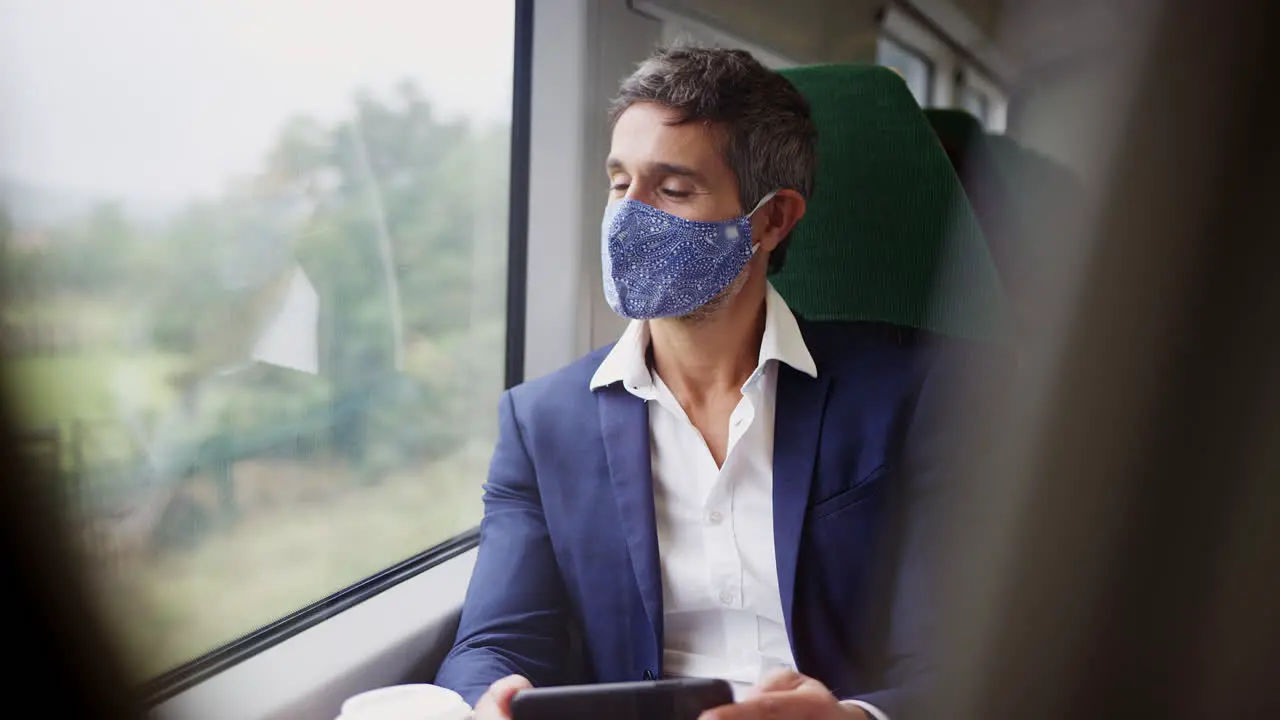 Businessman On Train Using Mobile Phone Wearing PPE Face Mask During Health Pandemic