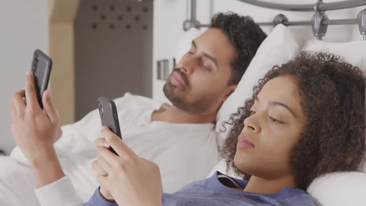 Couple In Bed Wearing Pyjamas Addicted To Using Mobile Phones Lying In Bed And Not Communicating