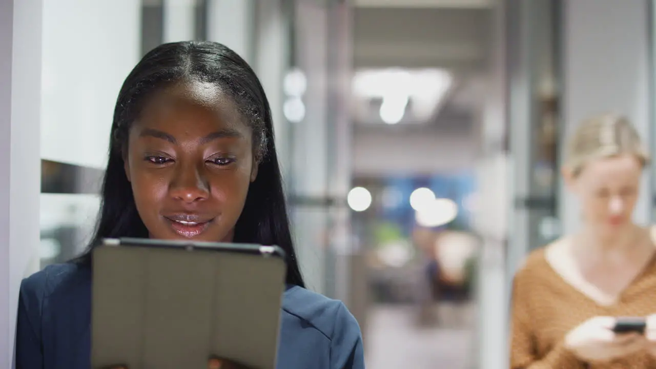 Evening Shot Of Young Businesswoman Standing In Corridor Of Modern Office Using Digital Tablet