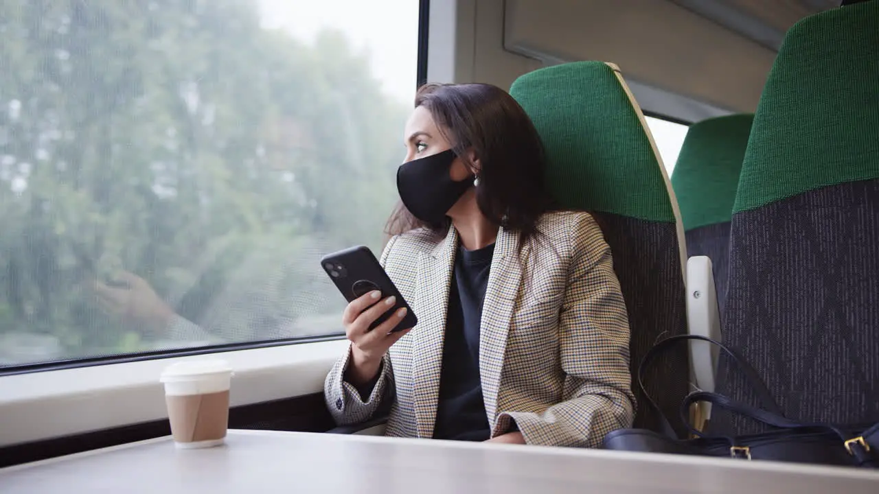 Businesswoman On Train Using Mobile Phone Wearing PPE Face Mask During Health Pandemic