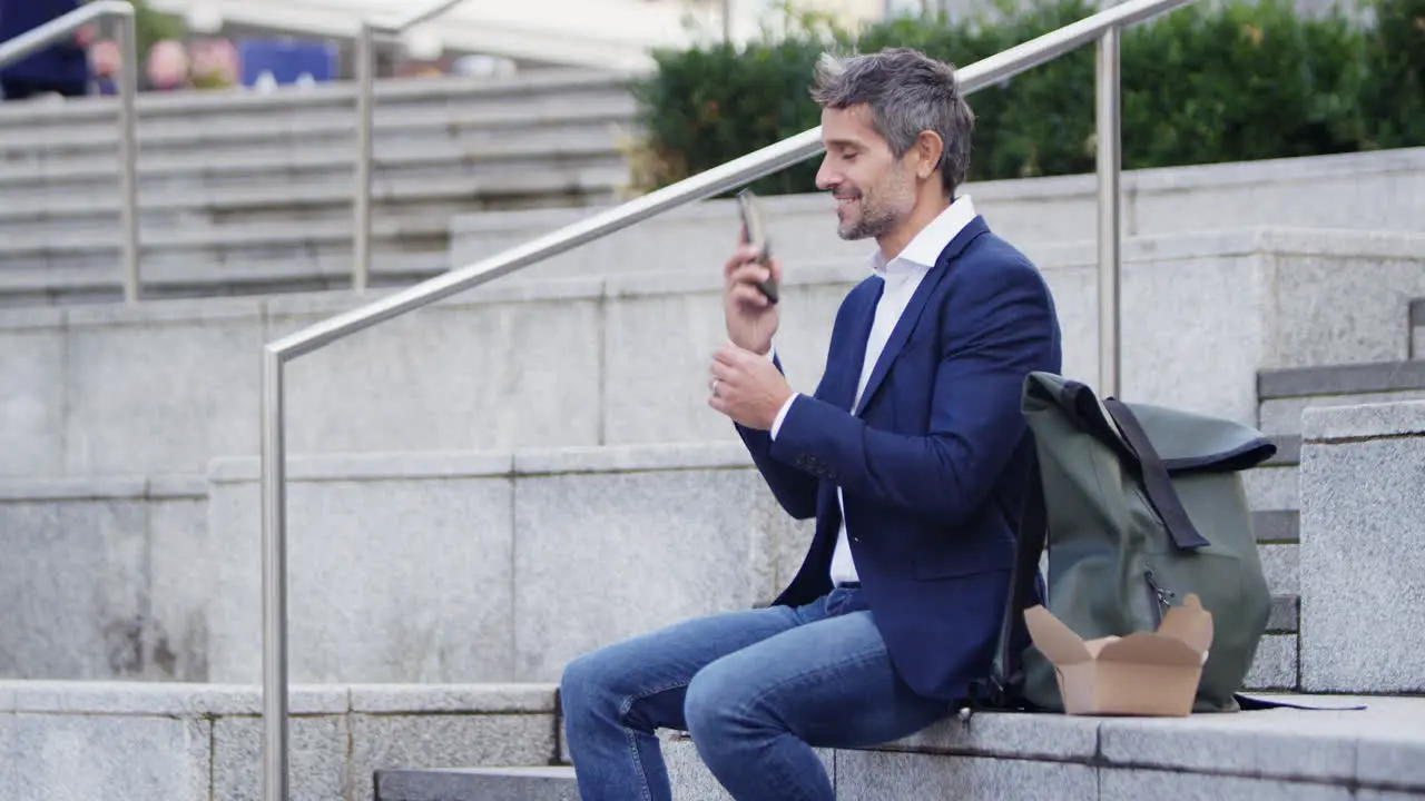 Businessman Sitting Outside On Lunch Break Talking On Mobile Phone