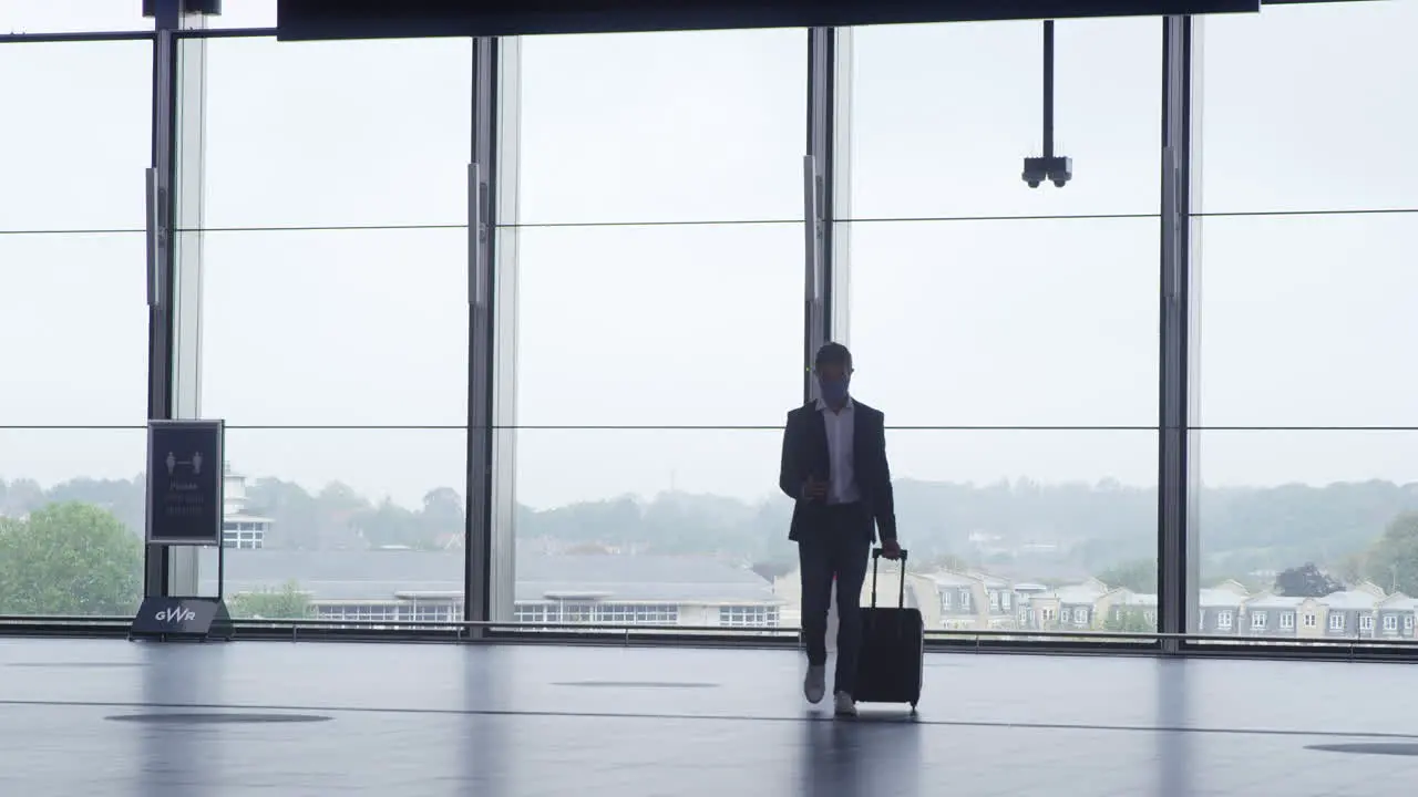 Businessman Walking Across Concourse At Railway Station With Mobile Phone Wearing PPE Face Mask