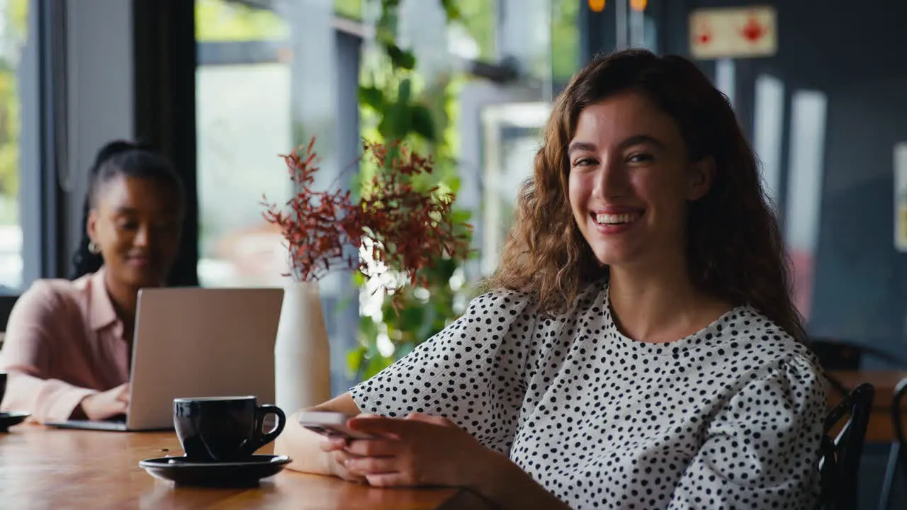 Portrait Of Smiling Young Businesswoman Sitting In Coffee Shop Using Mobile Phone