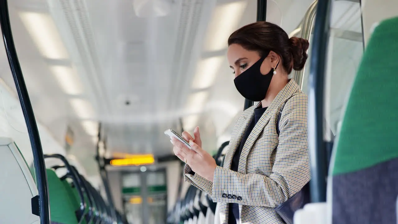 Businesswoman Stands In Train Carriage Using Mobile Phone Wearing PPE Face Masks During Pandemic