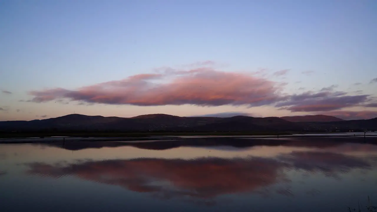 Perfect background and view from the shore of the water and the mountains in the background orange sky and clouds reflected in the water