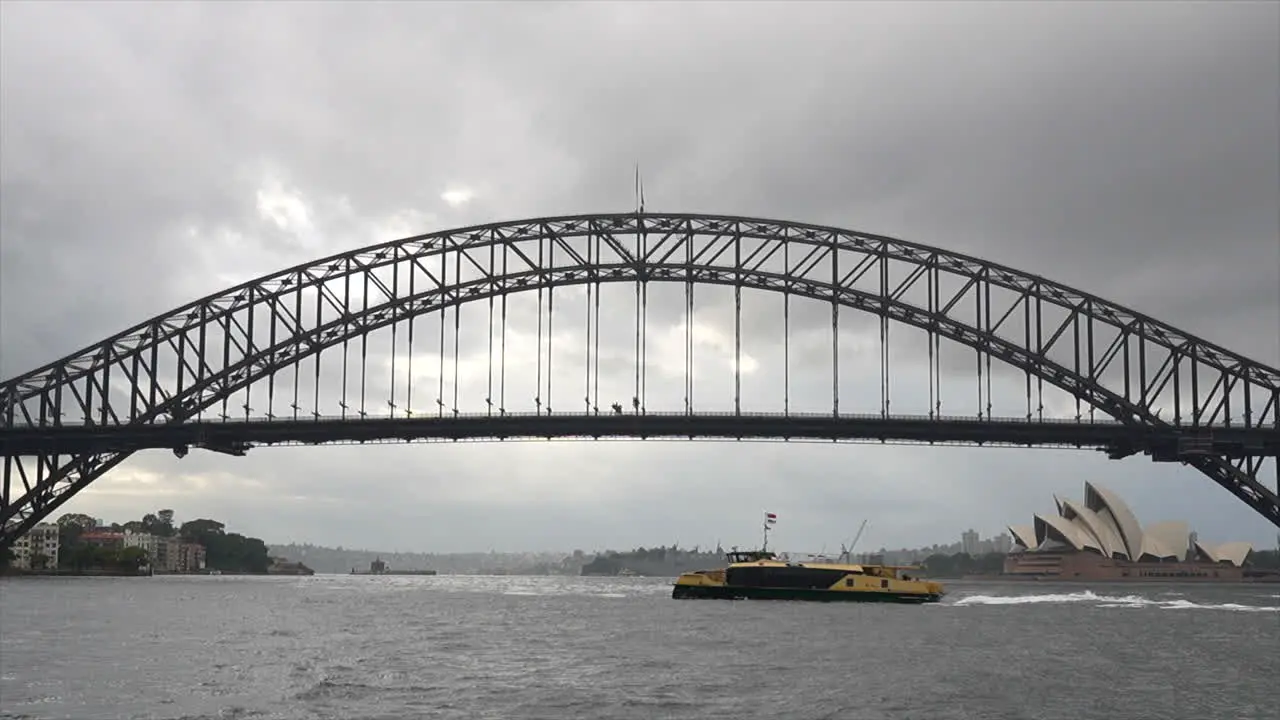 A ferry passes by Sydney harbour bridge and opera house on a rainy overcast day Australia