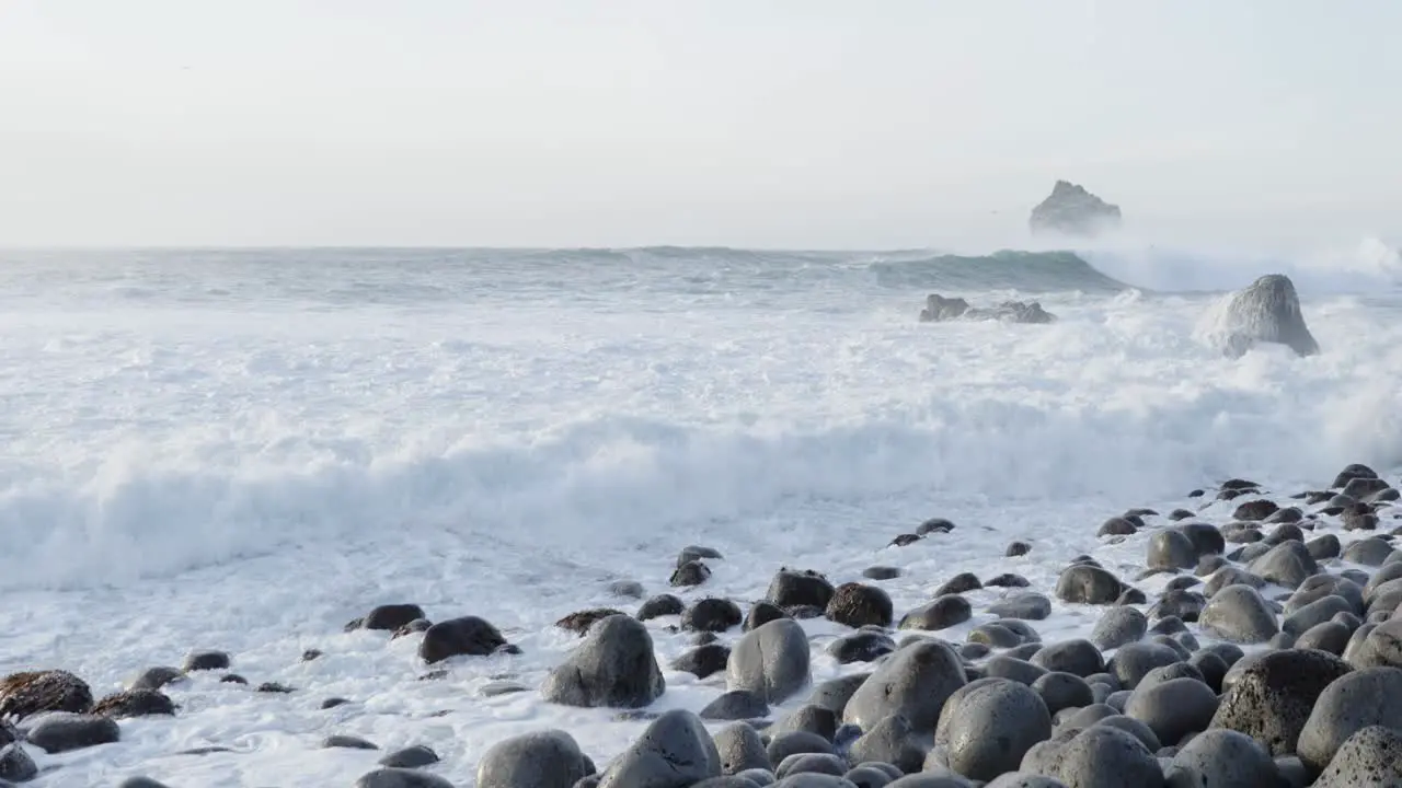 Crashing white foam waves on rocky boulder beach in Iceland slow motion