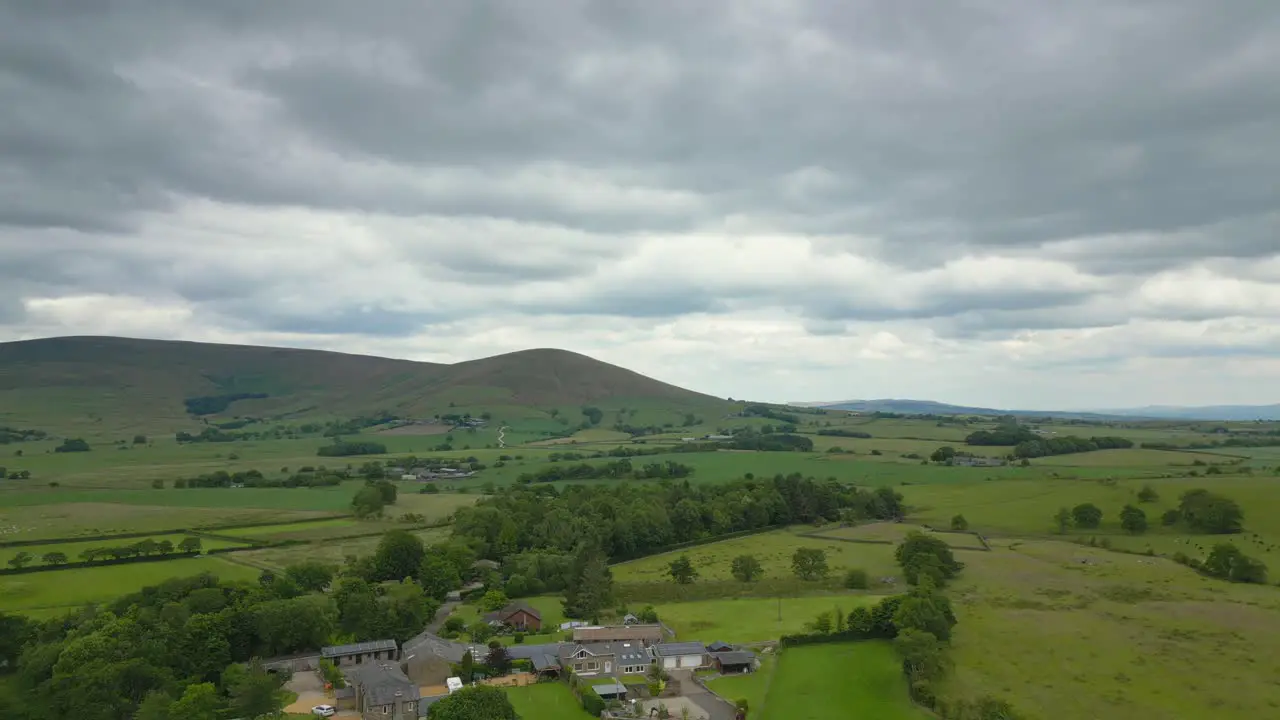 English countryside in summer with farmhouse flyover towards distant hills on overcast day