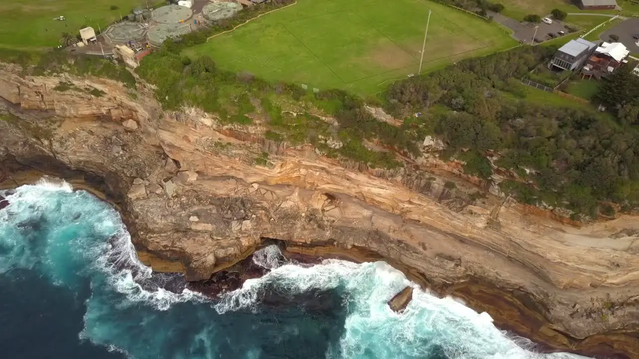 Epic drone shot of ocean waves smashing against cliff and rocks near a park Sydney Australia