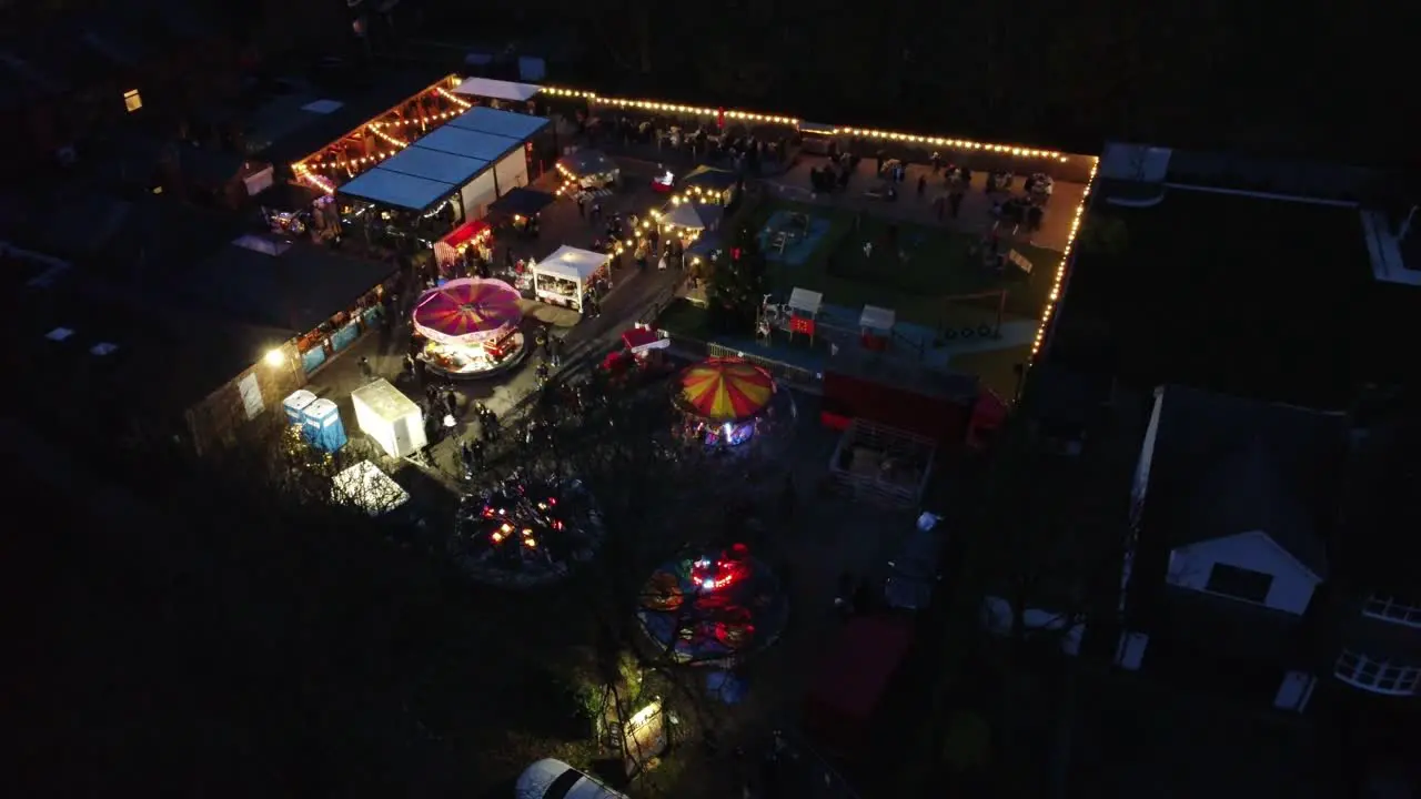 Illuminated Christmas fairground festival in neighbourhood pub car park at night aerial view