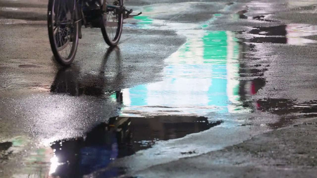 Reflection Of Person On Bicycle Seen At Puddle On Asphalt Road After Raining At Night In Tokyo Japan