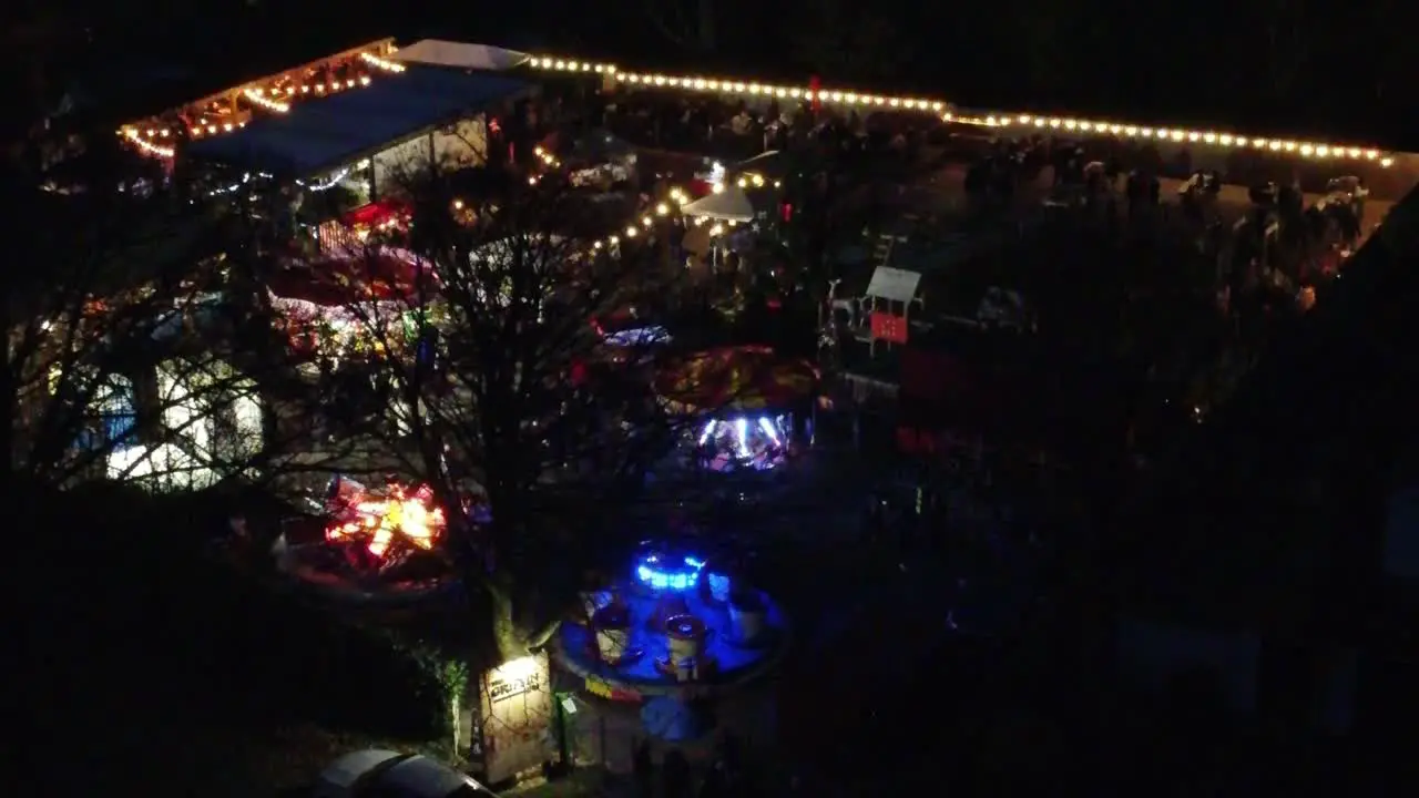 Illuminated festive Christmas fairground festival in neighbourhood car park at night aerial view