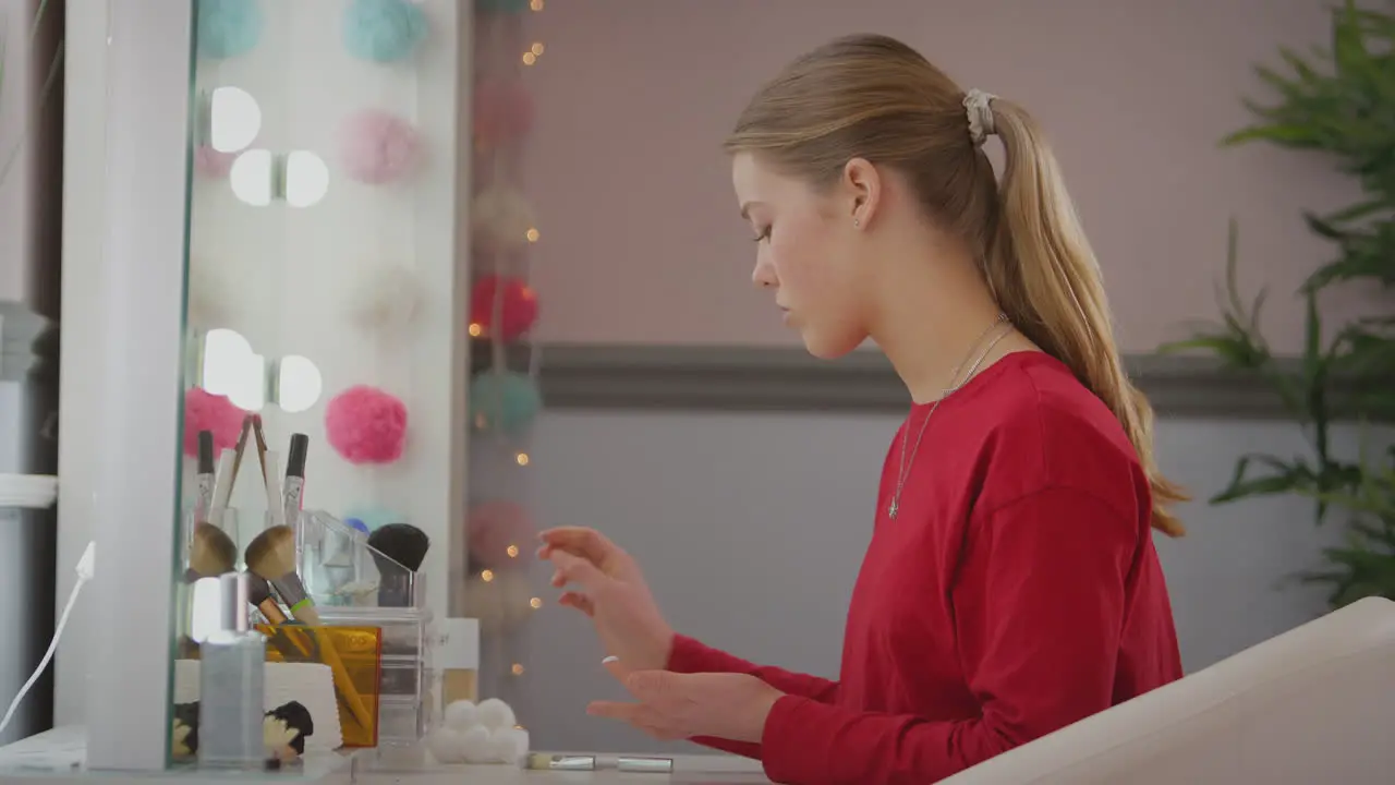 Teenage girl looking in mirror in bedroom at home taking off make up and moisturizing skin shot in slow motion