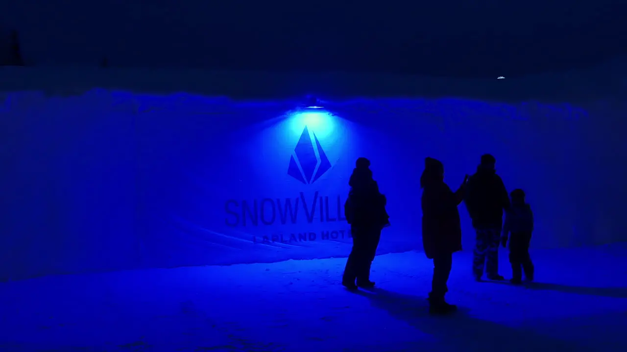 People Waiting Outside in Evening by Illuminated Entrance Sign for Snow Village Lapland Hotel