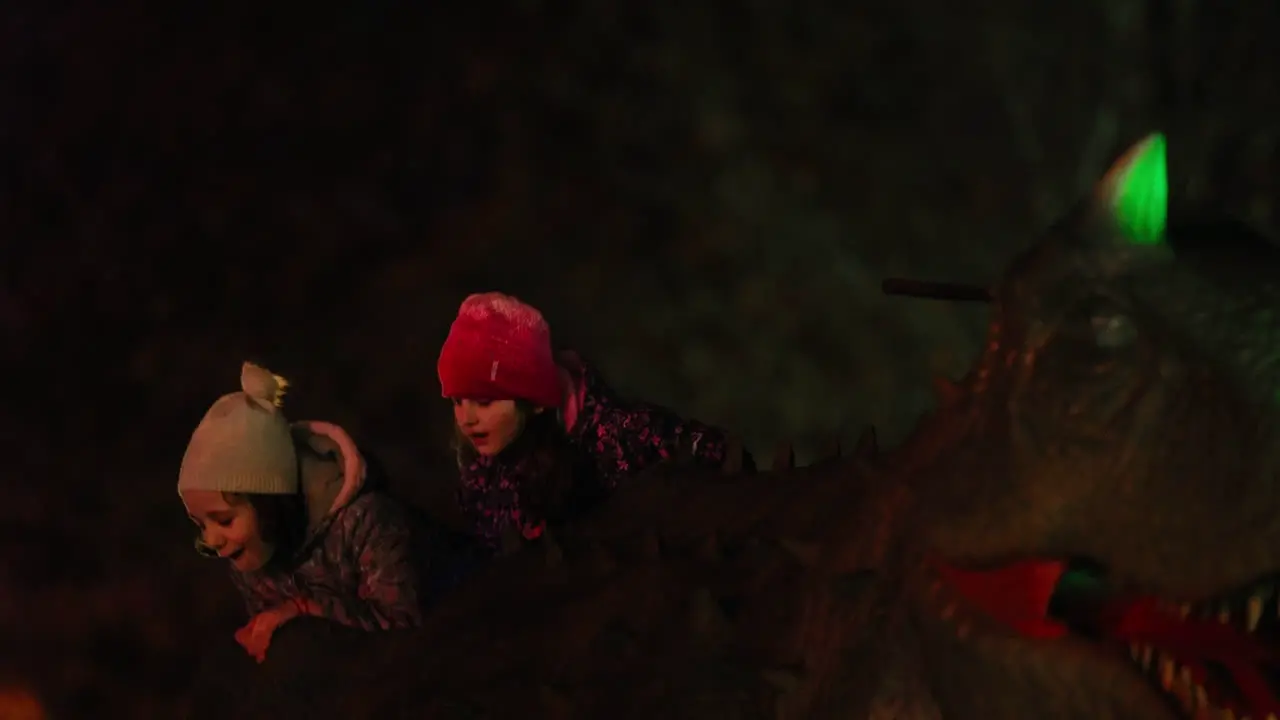 Two curious little girls having fun riding a dinosaur ride at an amusement parka at night time