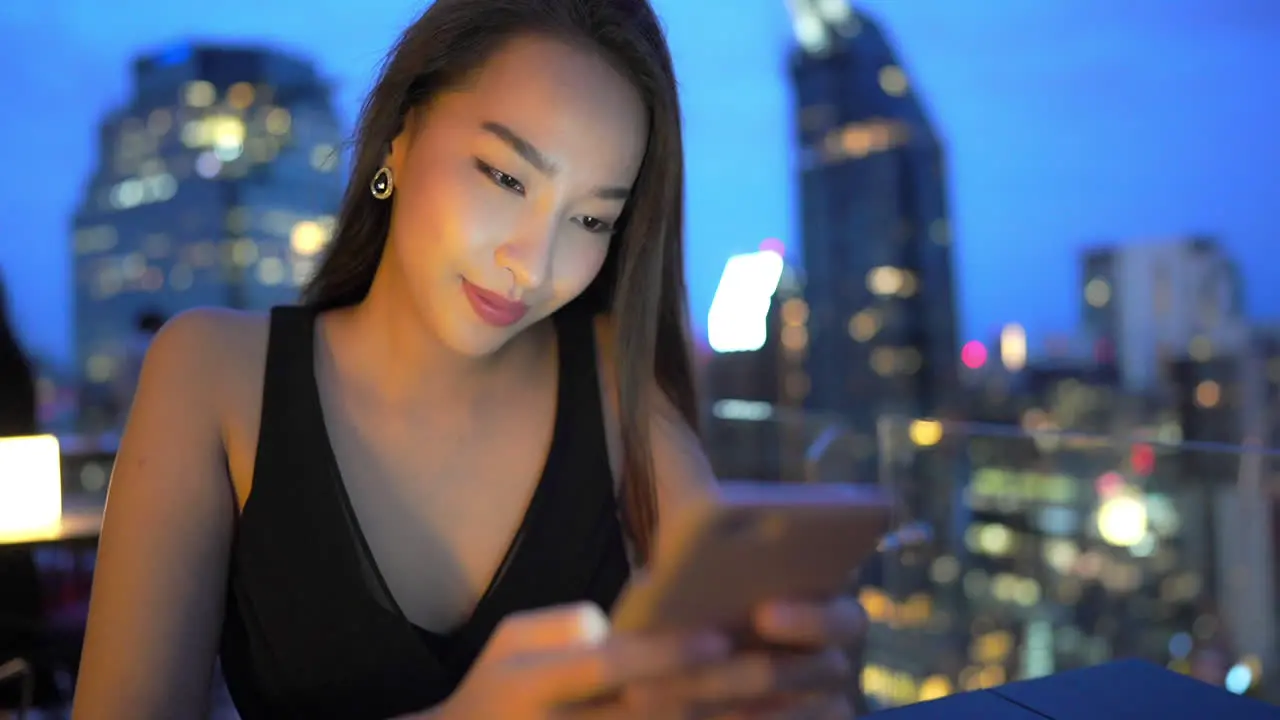 Attractive Trendy Asian Woman Using Smartphone on Rooftop Terrace Nighttime City Background CLOSE UP