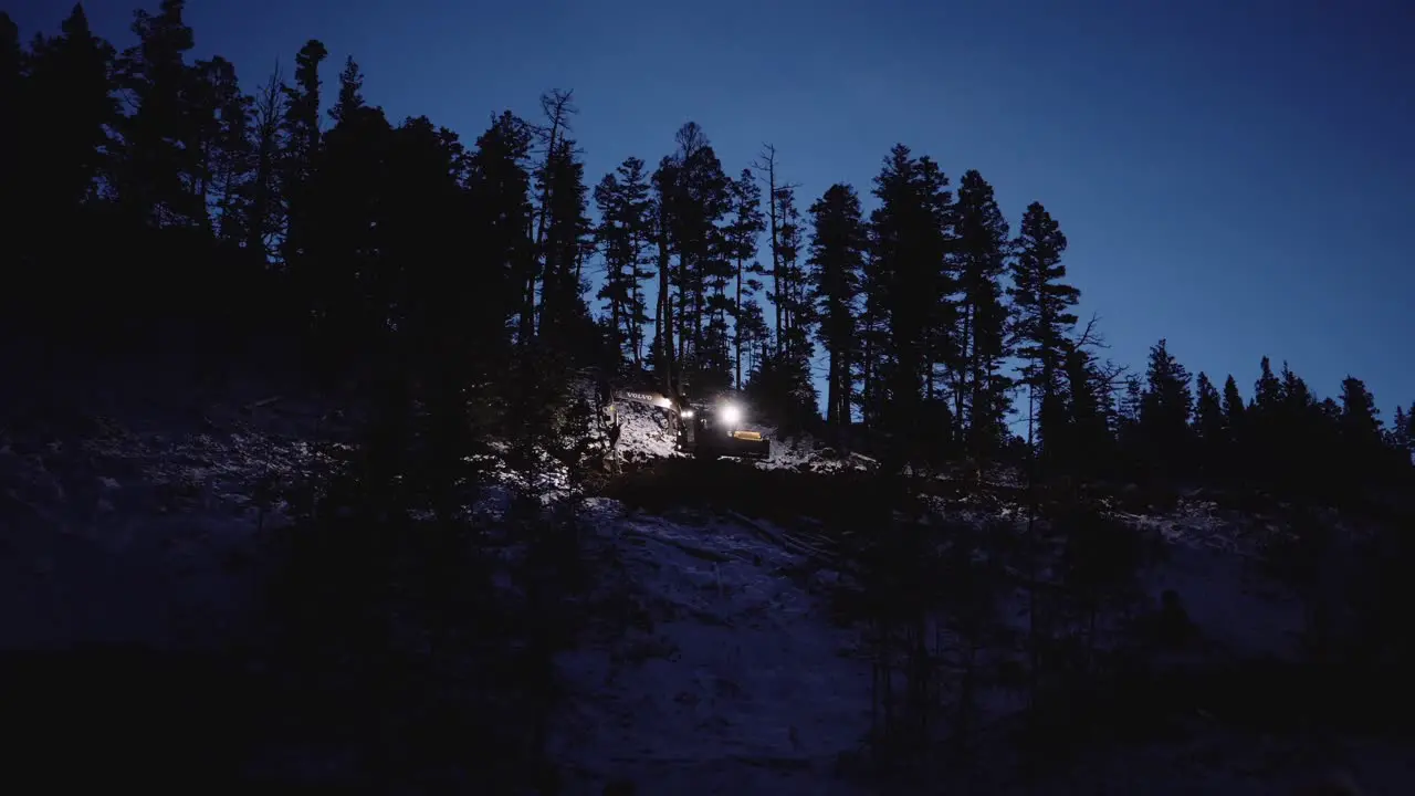 Wide far away establishing shot of nighttime industrial wood logging operation machinery moving around