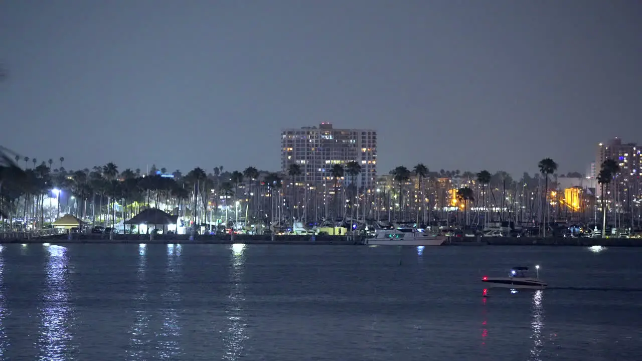 A boat makes its way across the bay at night with the lights of the city and harbor in the background