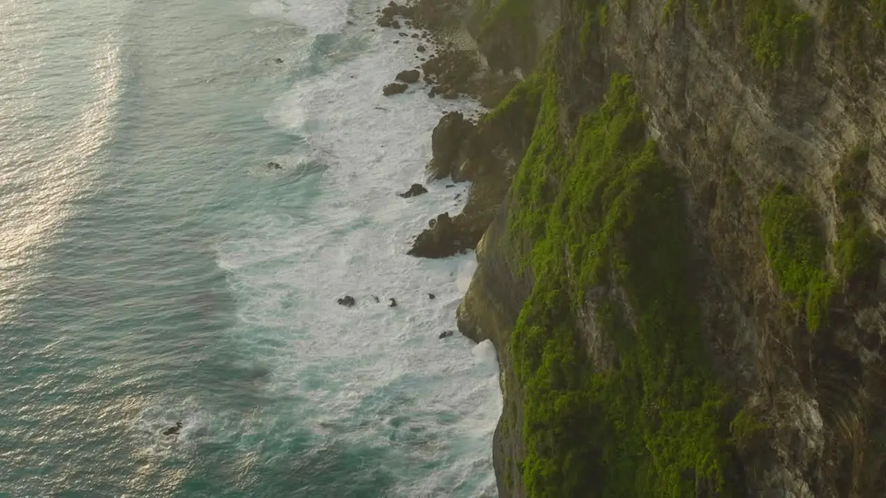 Rock cliffs with large swell waves crashing onto shore during sunset Nusa Penida aerial