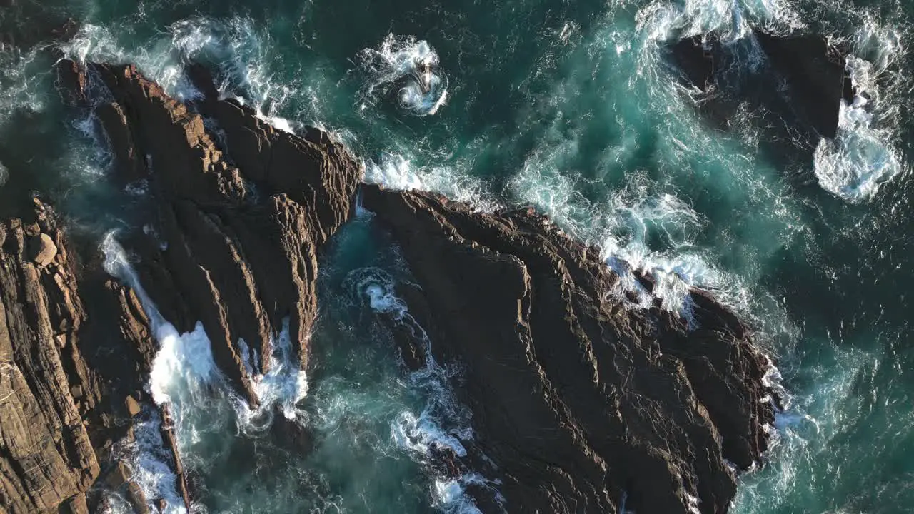 Rocky coast and rough sea water ocean waves aerial drone top down zoom out view