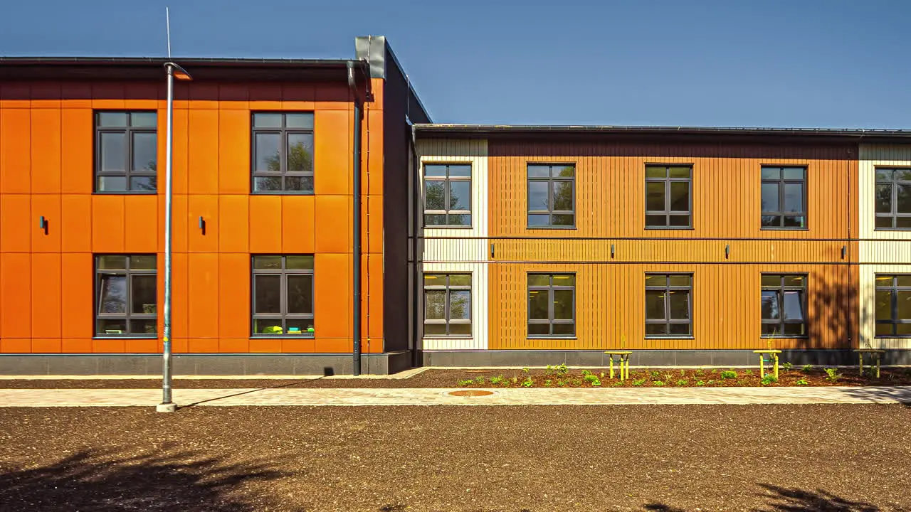 Timelapse of an orange building with symmetrical windows showcasing the shadows of vegetation in motion