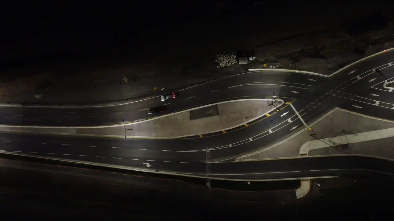 Aerial top down view traffic crossing illuminated Canadian twisting highway at night