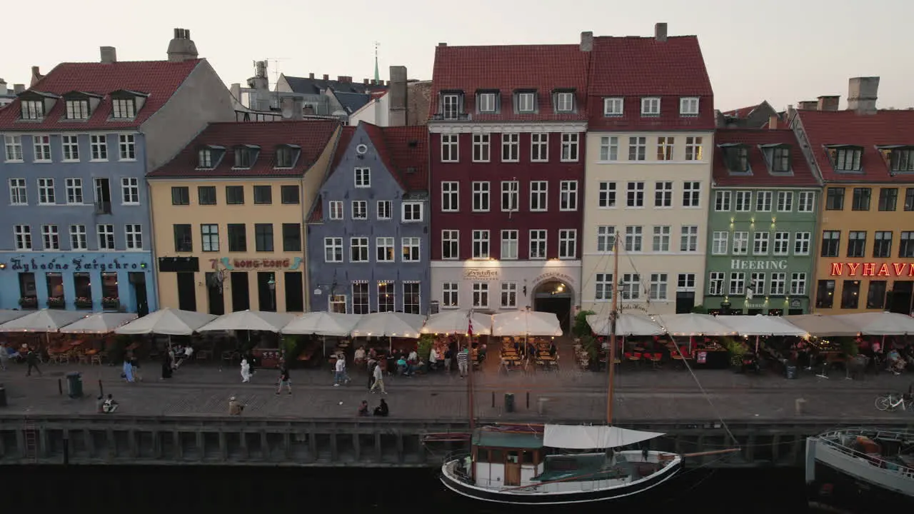 Experience the enchanting sunset over Nyhavn Copenhagen where people gather and boats navigate the charming canal