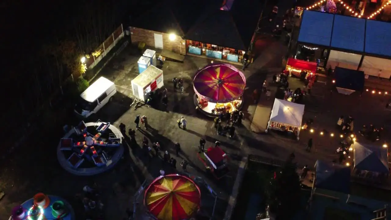 Illuminated Christmas fairground carnival in neighbourhood car park at night aerial view