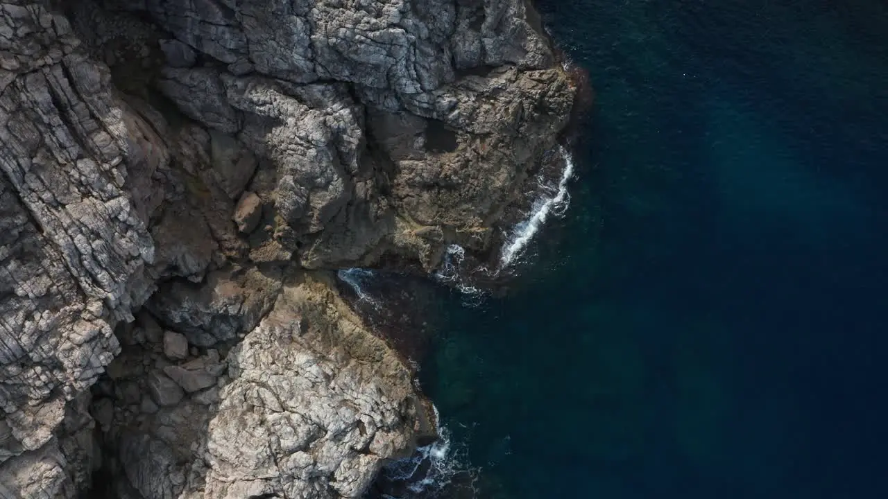 Drone Top Down Shot on Rocky Cliffside with waves crashing onto it