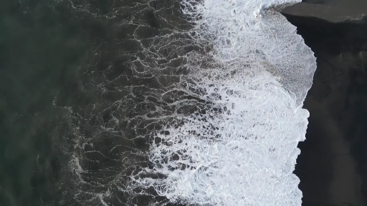 Birds eye view of waves crashing over a black sand beach in the south of Bali just after sunset aerial