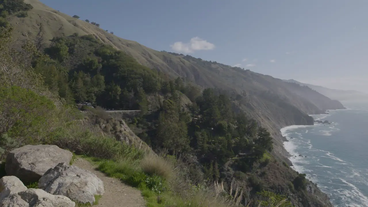 Panning shot from mountain side to the Pacific ocean at Big Sur California beach with waves crashing on a rocky shore