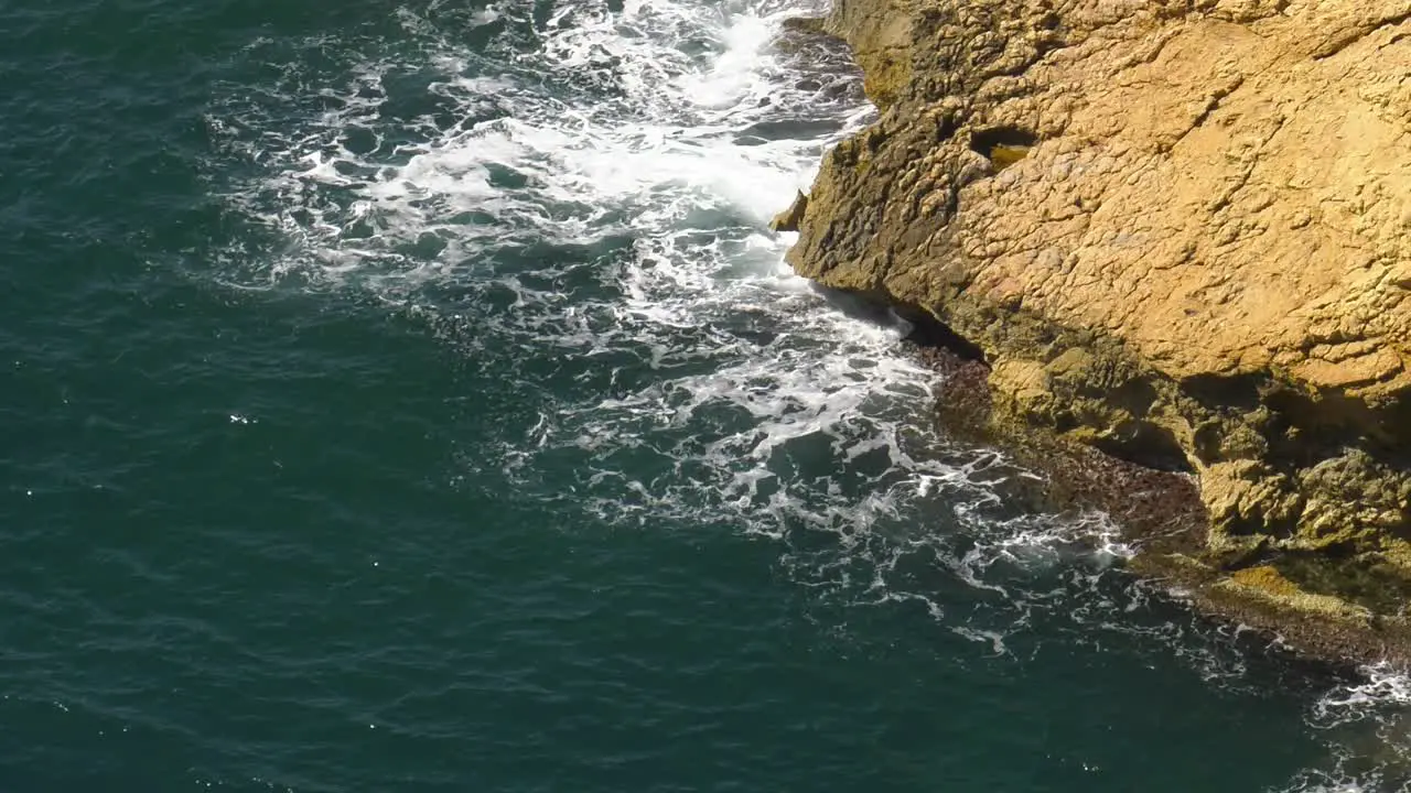 Rocky headland with blue ocean waves breaking in white foam slow motion