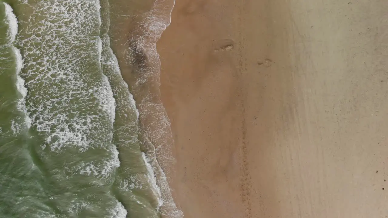 Aerial top down view of calm small waves crashing against the white undisturbed and isolated sand beach