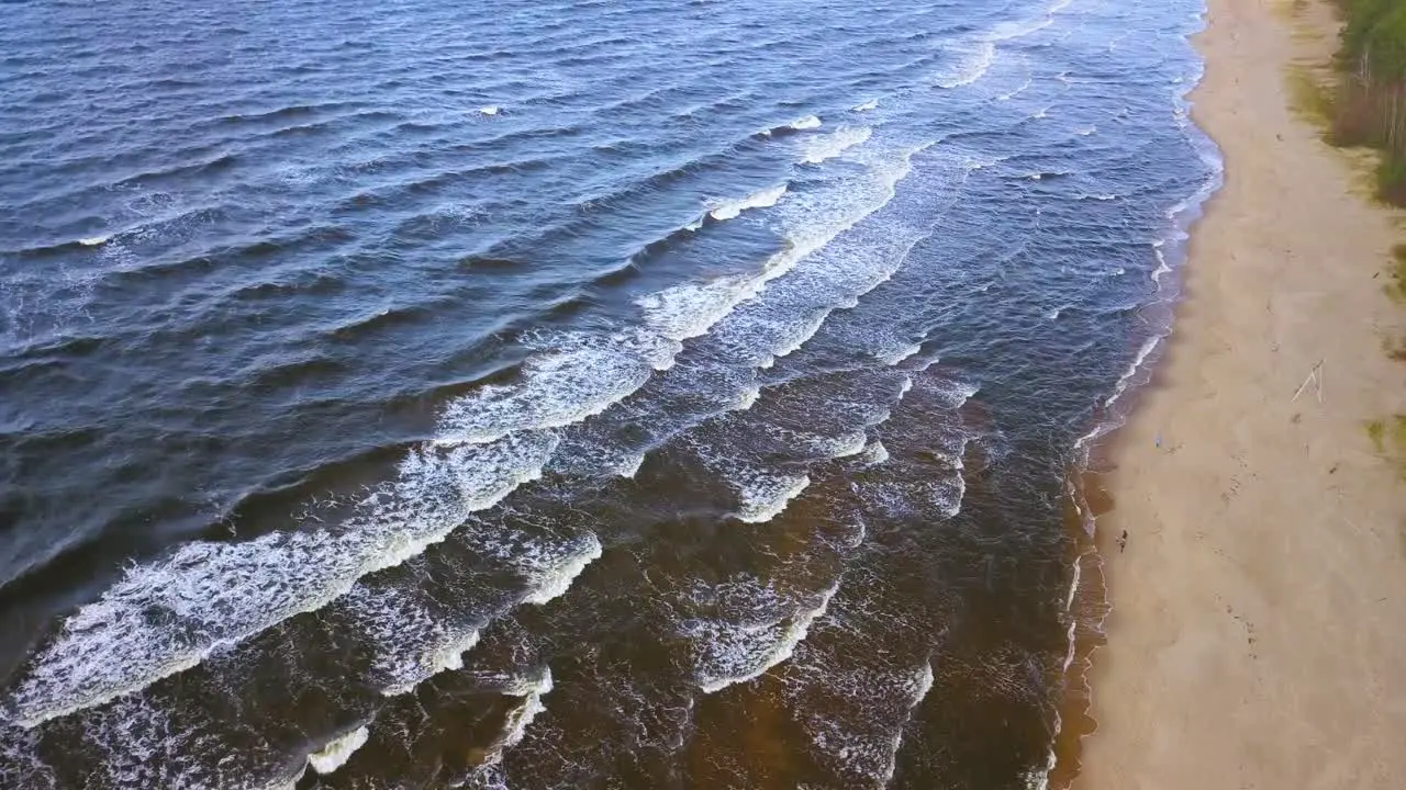 Aerial view of calm ocean waves reaching sandy coast on sunny day