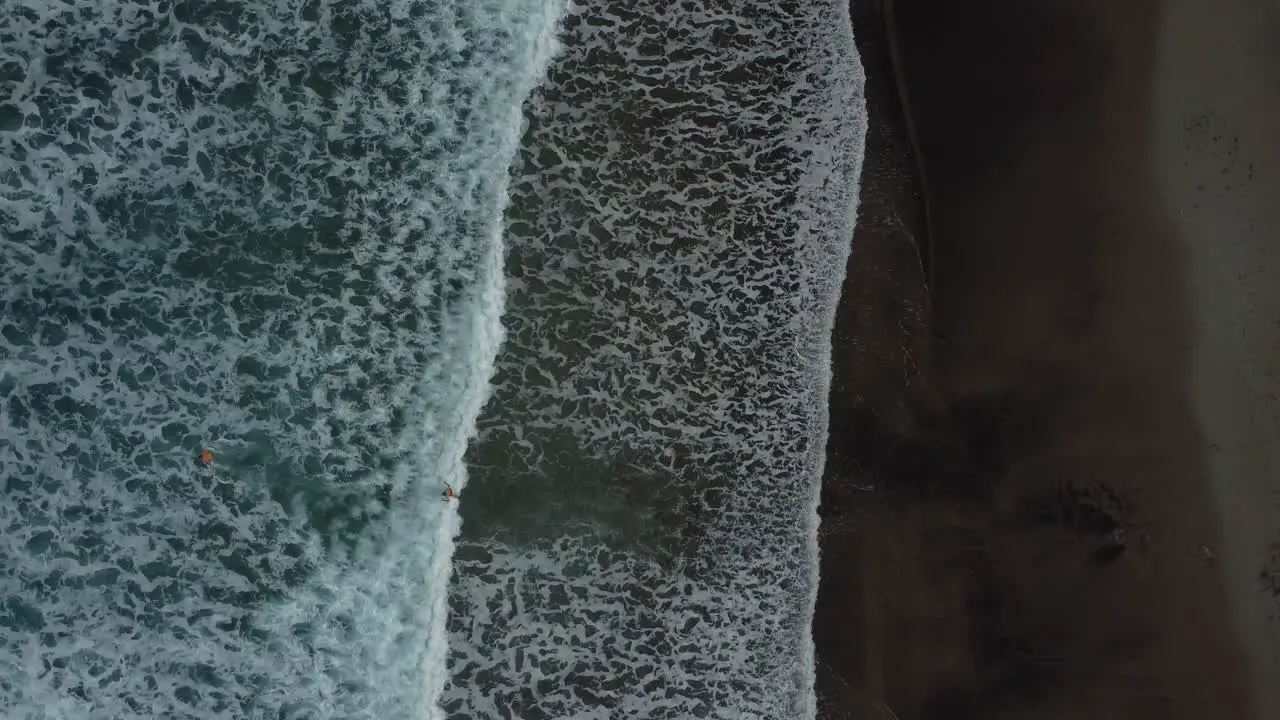 Aerial drone video looking down on volcanic black beach and waves in deep blue sea